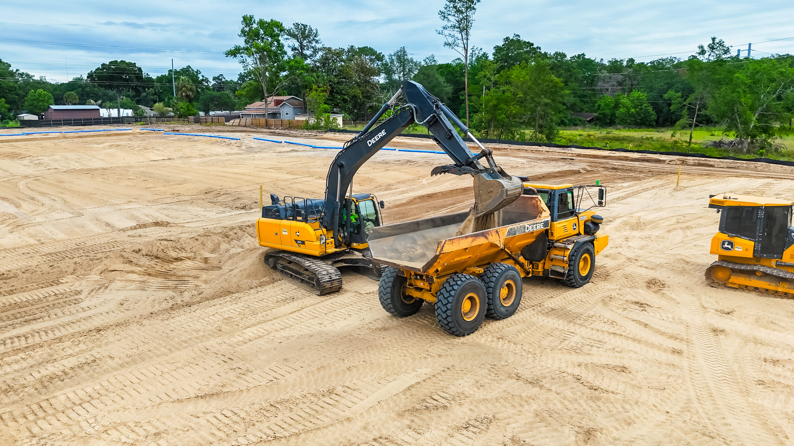 Drone view of John Deere excavator loading articulated dump truck on active grading site